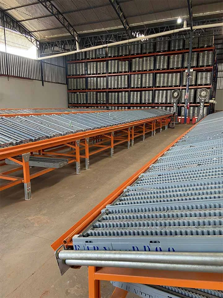 Linha de bancadas com roletes ROC GEO com caixas de testemunho, em galpão com estrutura porta-pallet ao fundo